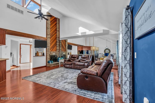 living room featuring ceiling fan, high vaulted ceiling, light hardwood / wood-style floors, and a brick fireplace