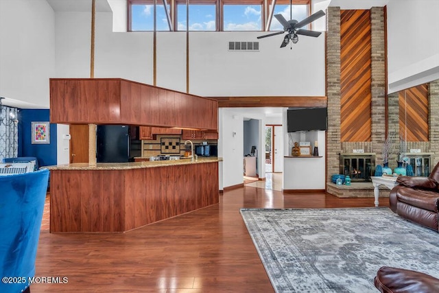 living room featuring dark wood-type flooring, ceiling fan, a brick fireplace, and a towering ceiling