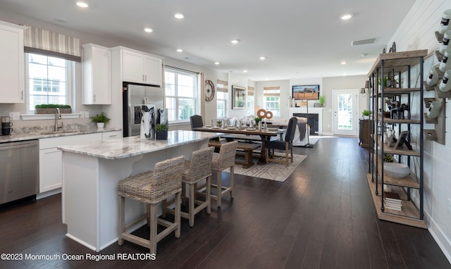 kitchen with a kitchen island, sink, white cabinets, light stone counters, and stainless steel appliances