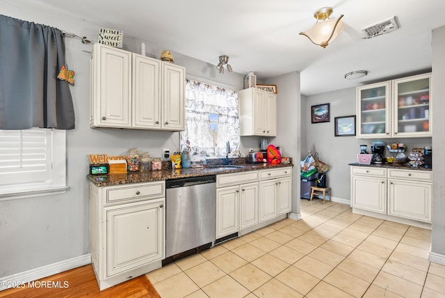 kitchen with sink, dishwasher, dark stone countertops, white cabinets, and light tile patterned flooring