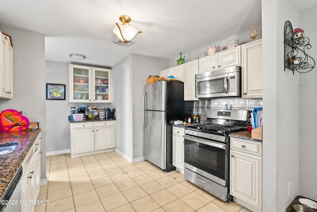 kitchen with light tile patterned floors, dark stone countertops, stainless steel appliances, white cabinets, and decorative backsplash