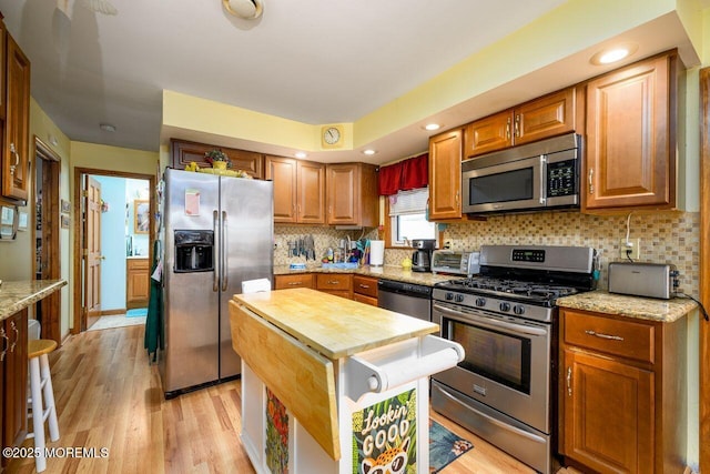 kitchen with light stone counters, backsplash, stainless steel appliances, and light hardwood / wood-style floors