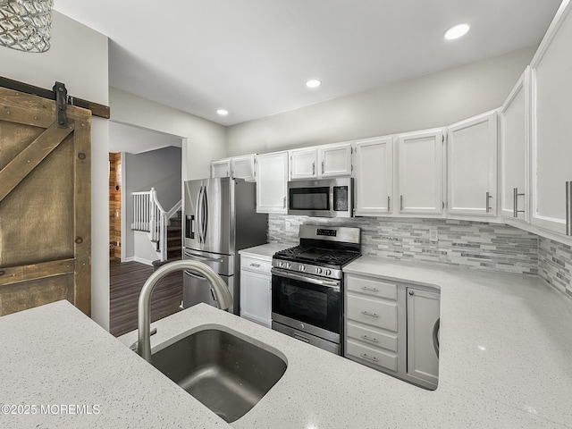 kitchen with tasteful backsplash, sink, white cabinets, stainless steel appliances, and a barn door