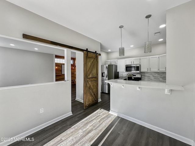 kitchen featuring appliances with stainless steel finishes, white cabinetry, backsplash, kitchen peninsula, and a barn door