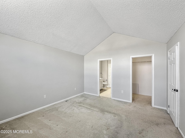 unfurnished bedroom featuring lofted ceiling, ensuite bathroom, light carpet, a spacious closet, and a closet