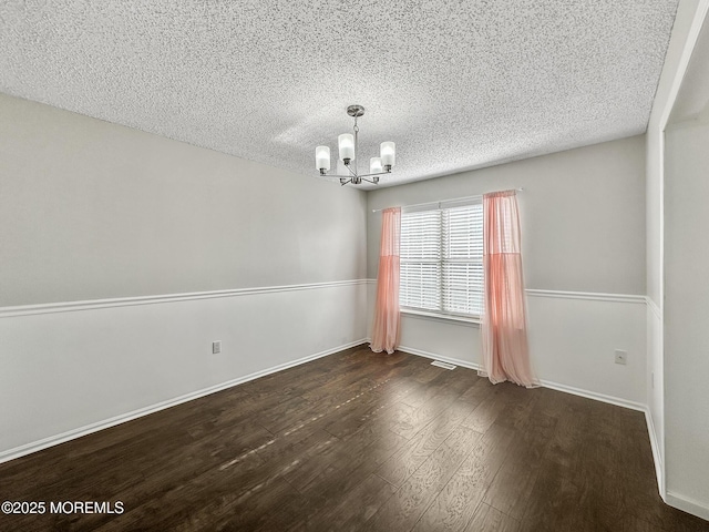 empty room with dark hardwood / wood-style flooring, a textured ceiling, and a chandelier