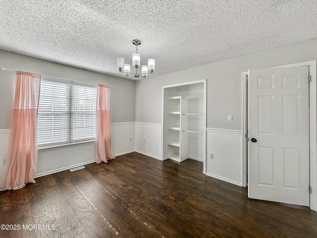 unfurnished dining area featuring an inviting chandelier, dark wood-type flooring, and a textured ceiling