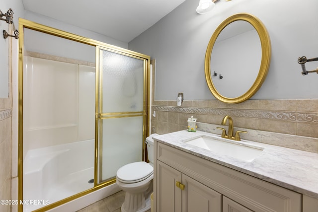 bathroom with tile walls, vanity, a shower with shower door, and toilet