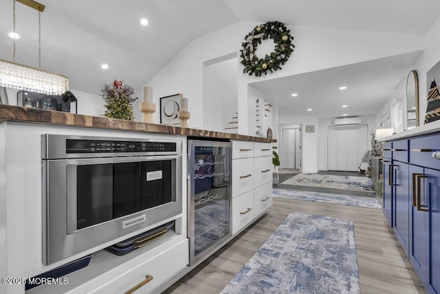 kitchen featuring pendant lighting, lofted ceiling, white cabinetry, wine cooler, and light hardwood / wood-style floors