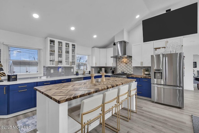 kitchen featuring appliances with stainless steel finishes, blue cabinets, a kitchen island, and wall chimney range hood