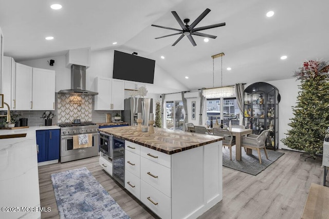 kitchen featuring a kitchen island, appliances with stainless steel finishes, white cabinetry, butcher block counters, and wall chimney range hood