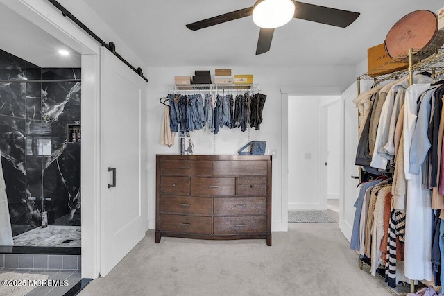 walk in closet with light carpet, a barn door, and ceiling fan