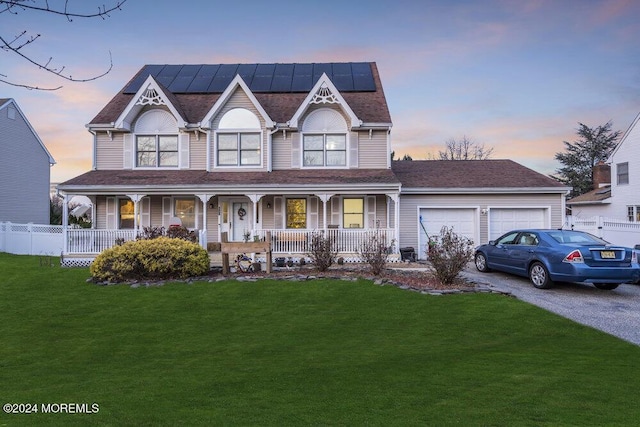 view of front of home with a garage, covered porch, a lawn, and solar panels