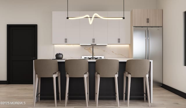 kitchen featuring tasteful backsplash, white cabinetry, a kitchen bar, and light wood-type flooring