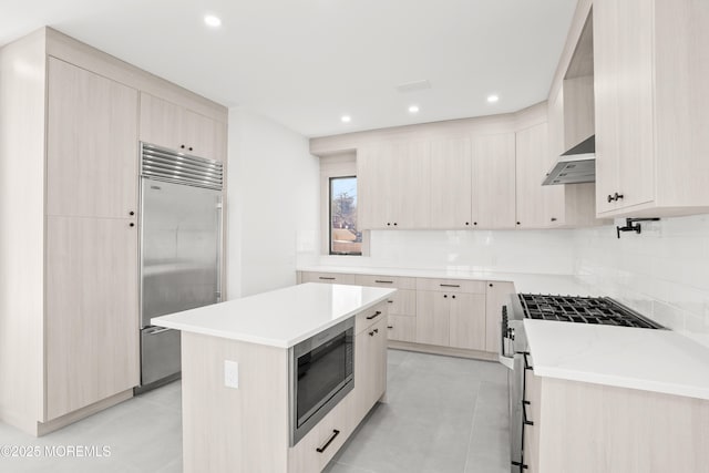 kitchen featuring built in appliances, light tile patterned floors, a kitchen island, and wall chimney range hood