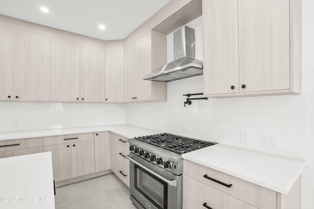 kitchen featuring high end stainless steel range oven, light stone countertops, light tile patterned floors, and wall chimney exhaust hood