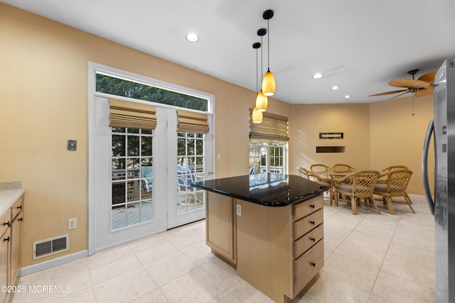 kitchen featuring light brown cabinetry, stainless steel refrigerator, decorative light fixtures, dark stone countertops, and a center island