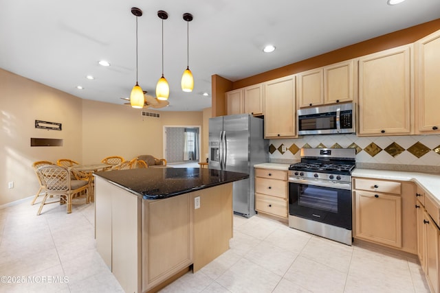 kitchen with light brown cabinetry, decorative light fixtures, a kitchen island, and appliances with stainless steel finishes