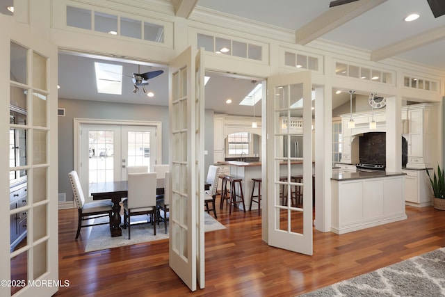 dining room with a skylight, beamed ceiling, dark hardwood / wood-style flooring, crown molding, and french doors