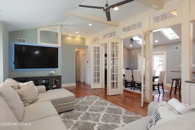 living room featuring crown molding, hardwood / wood-style flooring, ceiling fan, lofted ceiling with skylight, and french doors