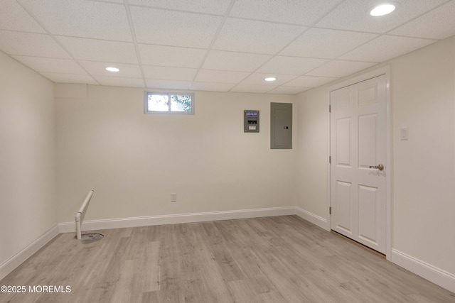 basement featuring electric panel, light hardwood / wood-style floors, and a drop ceiling