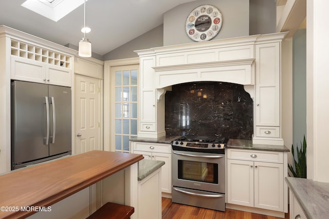 kitchen featuring appliances with stainless steel finishes, vaulted ceiling with skylight, pendant lighting, backsplash, and light wood-type flooring