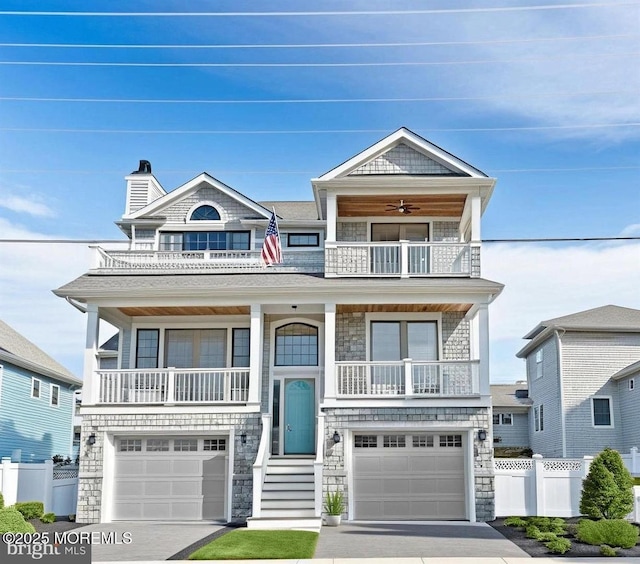 view of front facade with an attached garage, a ceiling fan, fence, a balcony, and driveway