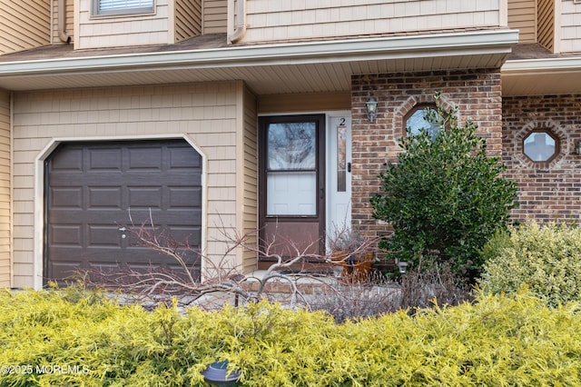 entrance to property featuring a garage and brick siding