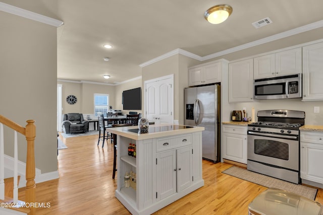 kitchen with a center island, light wood-type flooring, ornamental molding, appliances with stainless steel finishes, and white cabinets