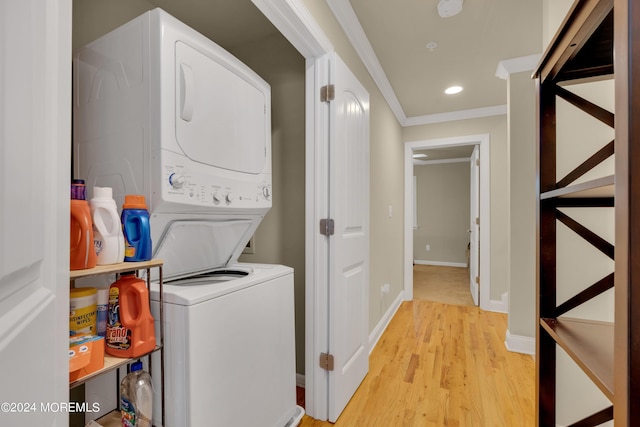 clothes washing area with stacked washing maching and dryer, crown molding, and light hardwood / wood-style flooring