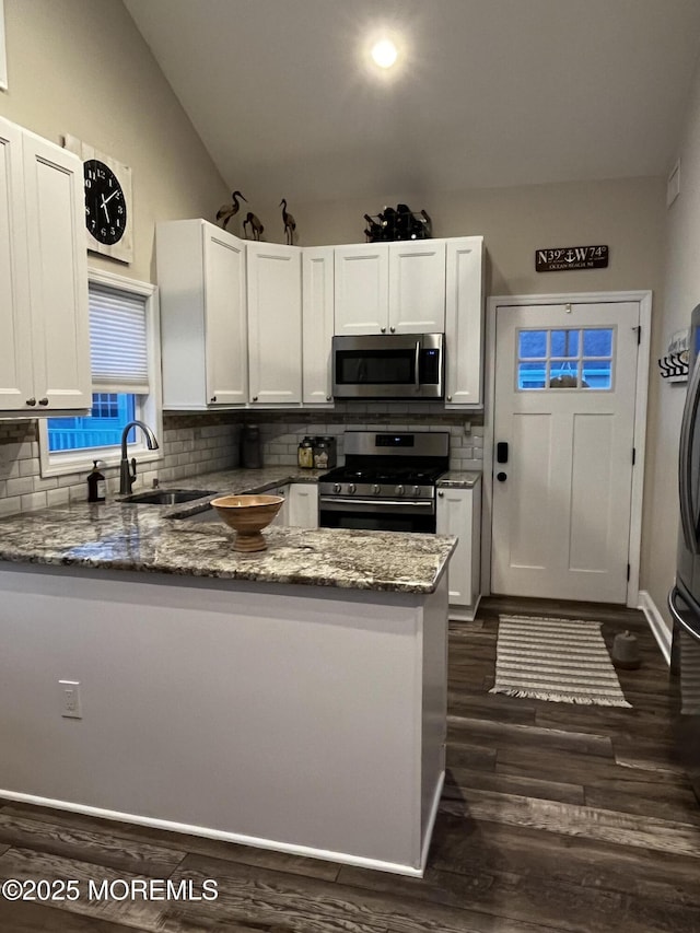 kitchen with sink, white cabinets, dark stone counters, kitchen peninsula, and stainless steel appliances