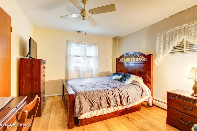 bedroom with ceiling fan, a baseboard heating unit, and light wood-type flooring