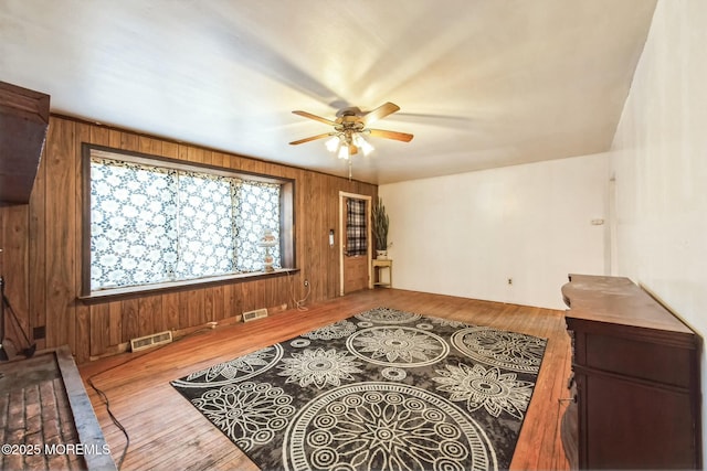 living room featuring ceiling fan, wood-type flooring, and wood walls