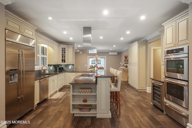 kitchen with appliances with stainless steel finishes, island range hood, a kitchen breakfast bar, kitchen peninsula, and cream cabinetry