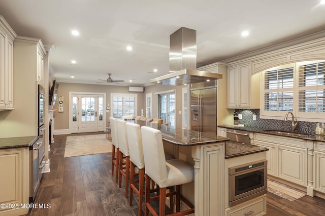 kitchen with sink, island range hood, a center island, dark stone countertops, and stainless steel appliances