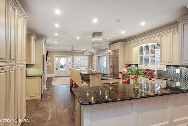 kitchen with island range hood, a center island, appliances with stainless steel finishes, dark stone counters, and cream cabinets