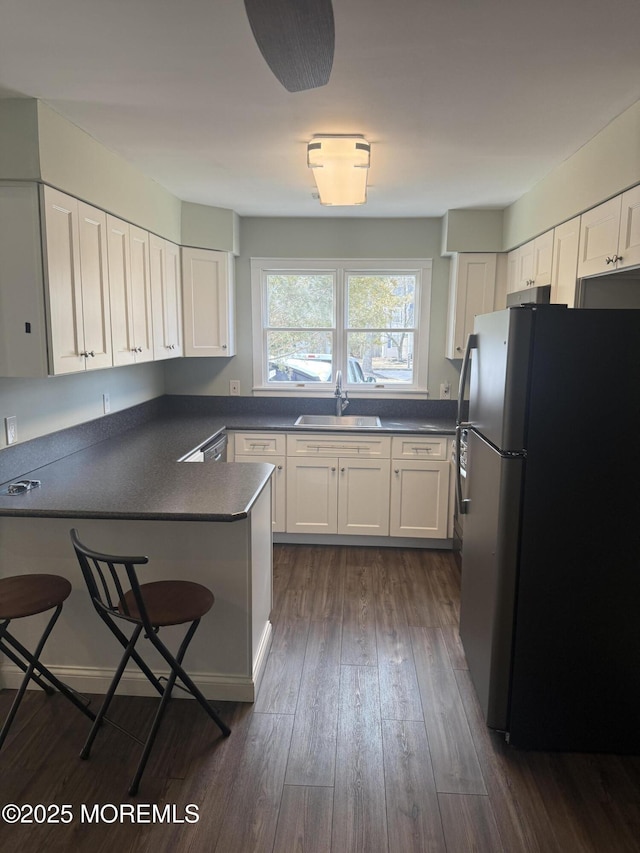 kitchen featuring a kitchen bar, sink, stainless steel refrigerator, dark hardwood / wood-style floors, and white cabinets