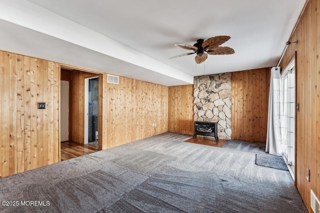 unfurnished living room featuring ceiling fan, wooden walls, and carpet flooring