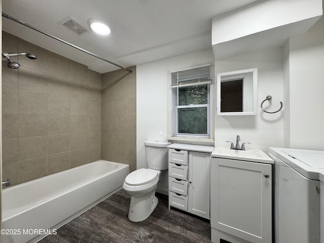 full bathroom featuring vanity, wood-type flooring, tiled shower / bath, washer / dryer, and toilet