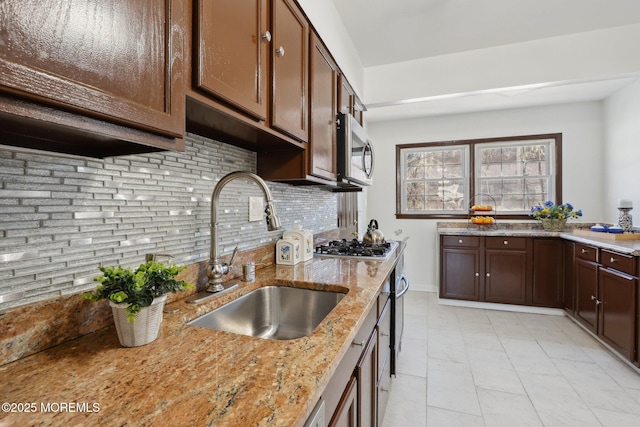 kitchen with appliances with stainless steel finishes, sink, backsplash, light stone countertops, and dark brown cabinets