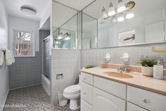 full bathroom featuring tile walls, enclosed tub / shower combo, vanity, ceiling fan, and toilet