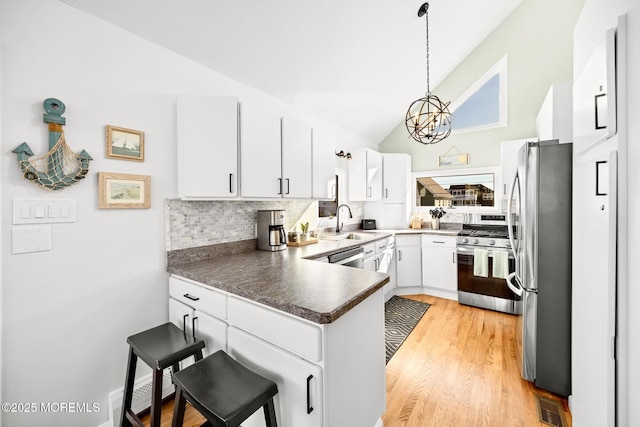 kitchen featuring appliances with stainless steel finishes, decorative light fixtures, white cabinetry, a kitchen bar, and kitchen peninsula