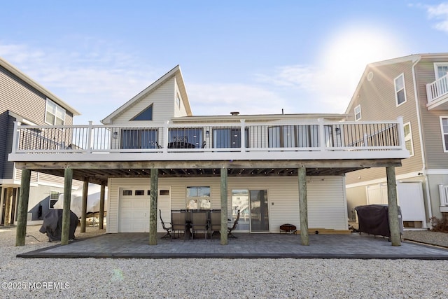 rear view of house featuring a wooden deck, a garage, and a patio