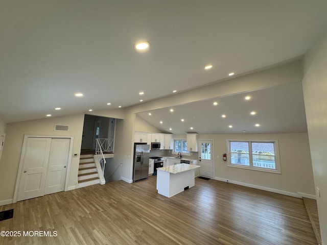 kitchen with vaulted ceiling, a kitchen island, appliances with stainless steel finishes, white cabinetry, and light hardwood / wood-style floors