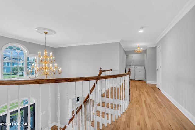 corridor with an inviting chandelier, washing machine and clothes dryer, crown molding, and light wood-type flooring