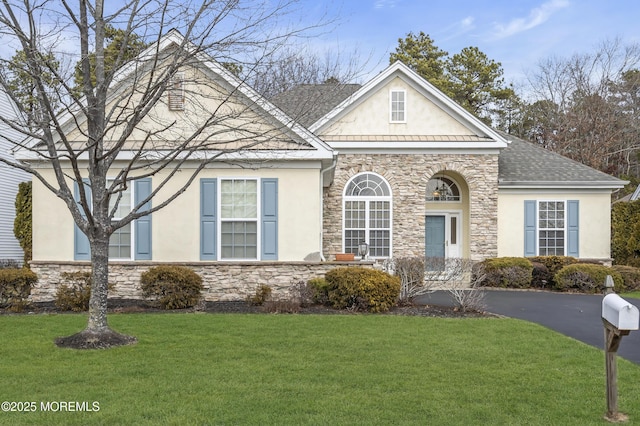 view of front facade featuring stone siding, roof with shingles, a front yard, and stucco siding