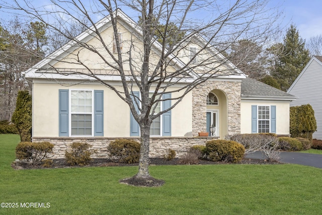 view of front of property featuring stone siding, roof with shingles, a front yard, and stucco siding