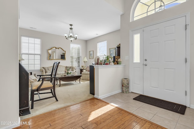 entrance foyer with baseboards, light wood-type flooring, visible vents, and an inviting chandelier