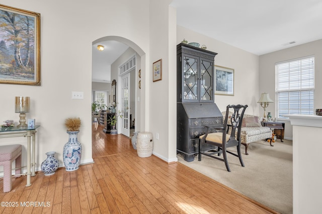 office space featuring arched walkways, visible vents, light wood-style flooring, and baseboards