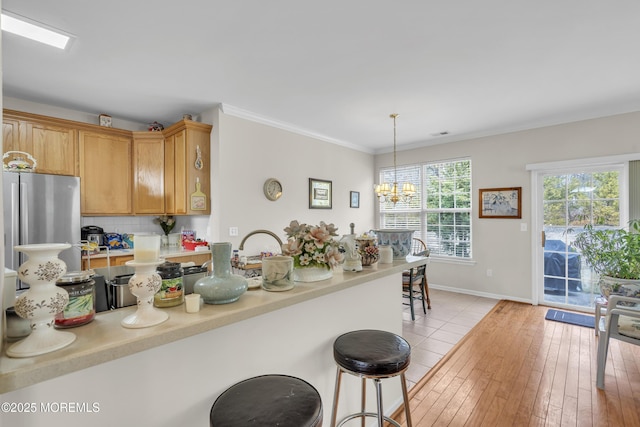 kitchen with crown molding, light wood finished floors, light countertops, freestanding refrigerator, and a chandelier